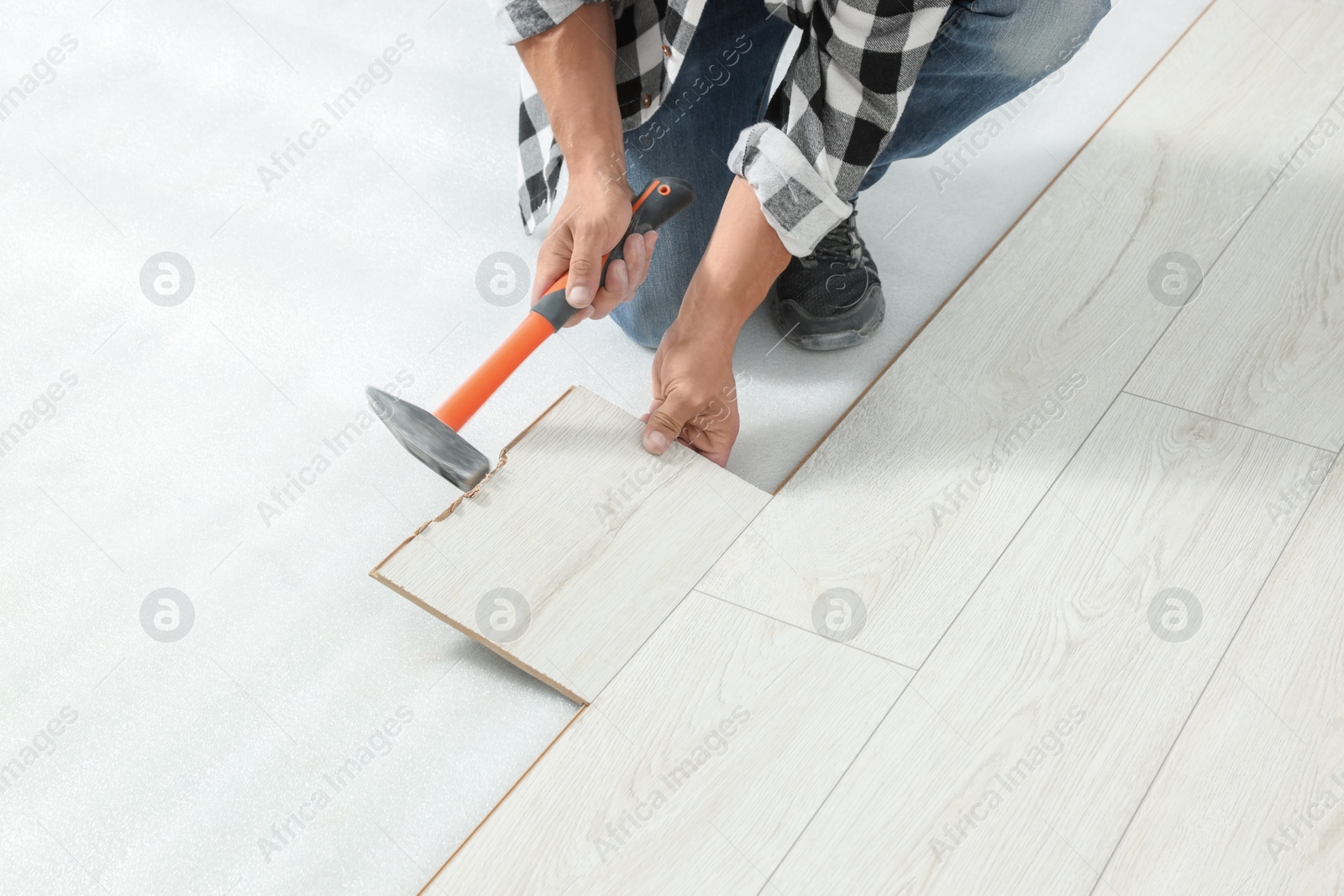 Photo of Professional worker using hammer during installation of new laminate flooring, closeup