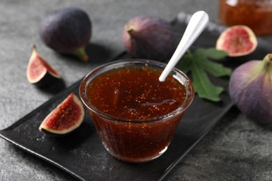 Photo of Glass bowl with tasty sweet jam and fresh figs on grey table, closeup