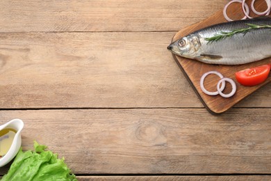 Photo of Board with delicious salted herring, onion, tomato, lettuce and olive oil on wooden table, flat lay. Space for text