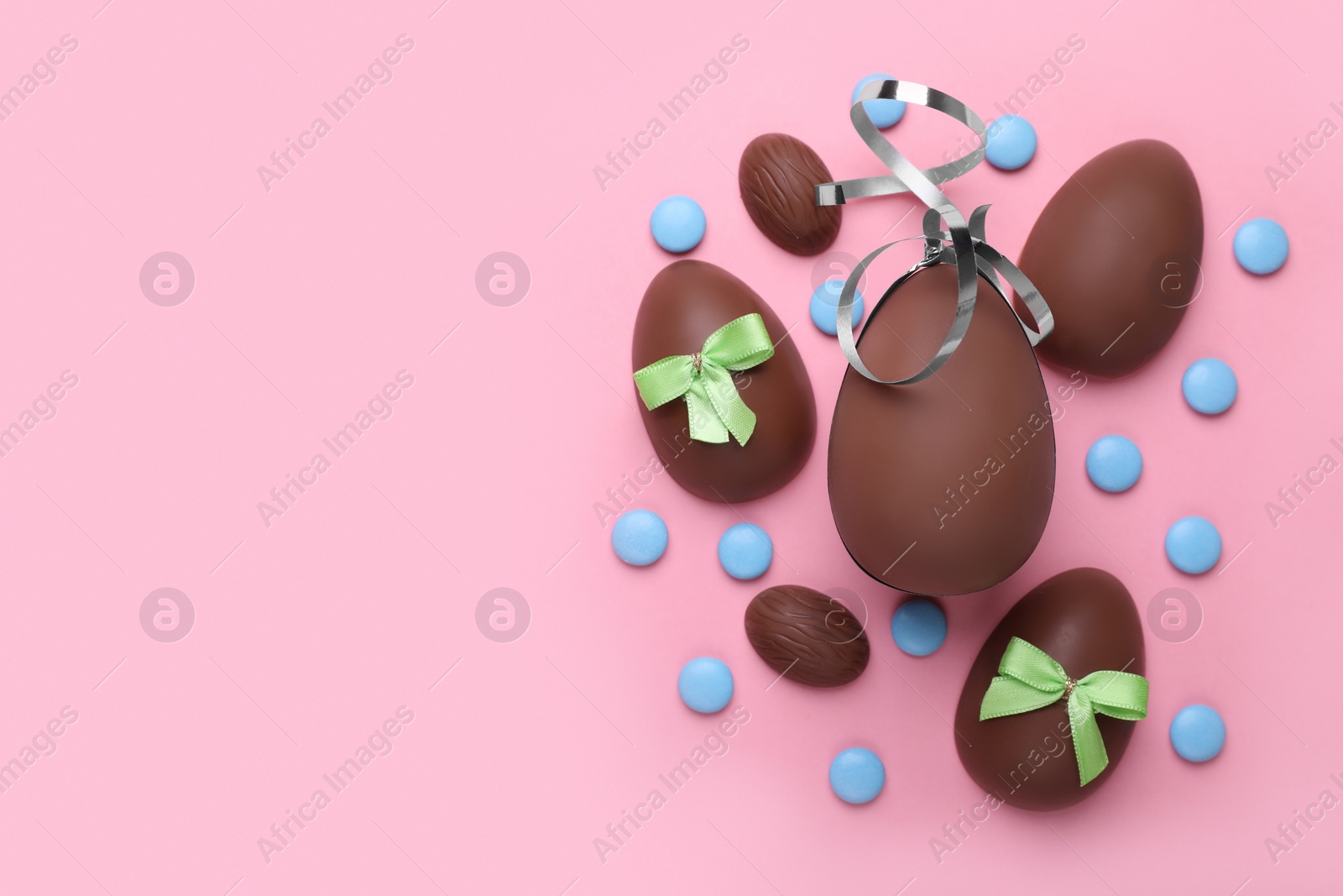 Delicious chocolate eggs with bows and candies on pink background, flat lay. Space for text Photo of Delicious chocolate eggs with bows and candies on pink background, flat lay. Space for text