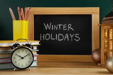 Chalkboard with text Winter Holidays and school supplies on wooden table