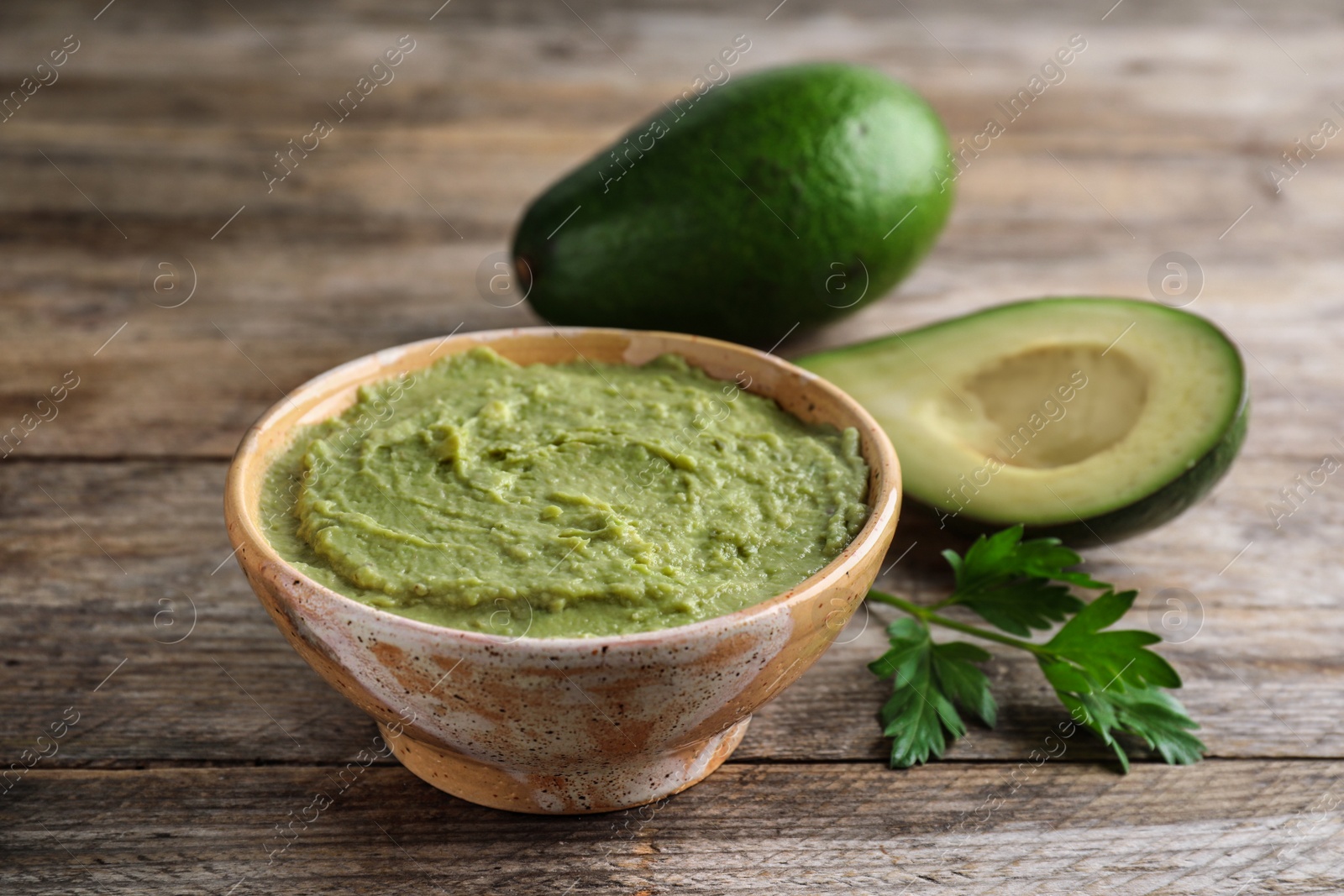 Photo of Bowl with guacamole and ripe avocados served on brown wooden table