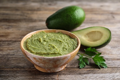 Photo of Bowl with guacamole and ripe avocados served on brown wooden table