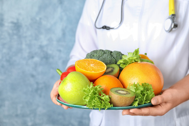 Female nutritionist with fruits and vegetables on light blue background, closeup