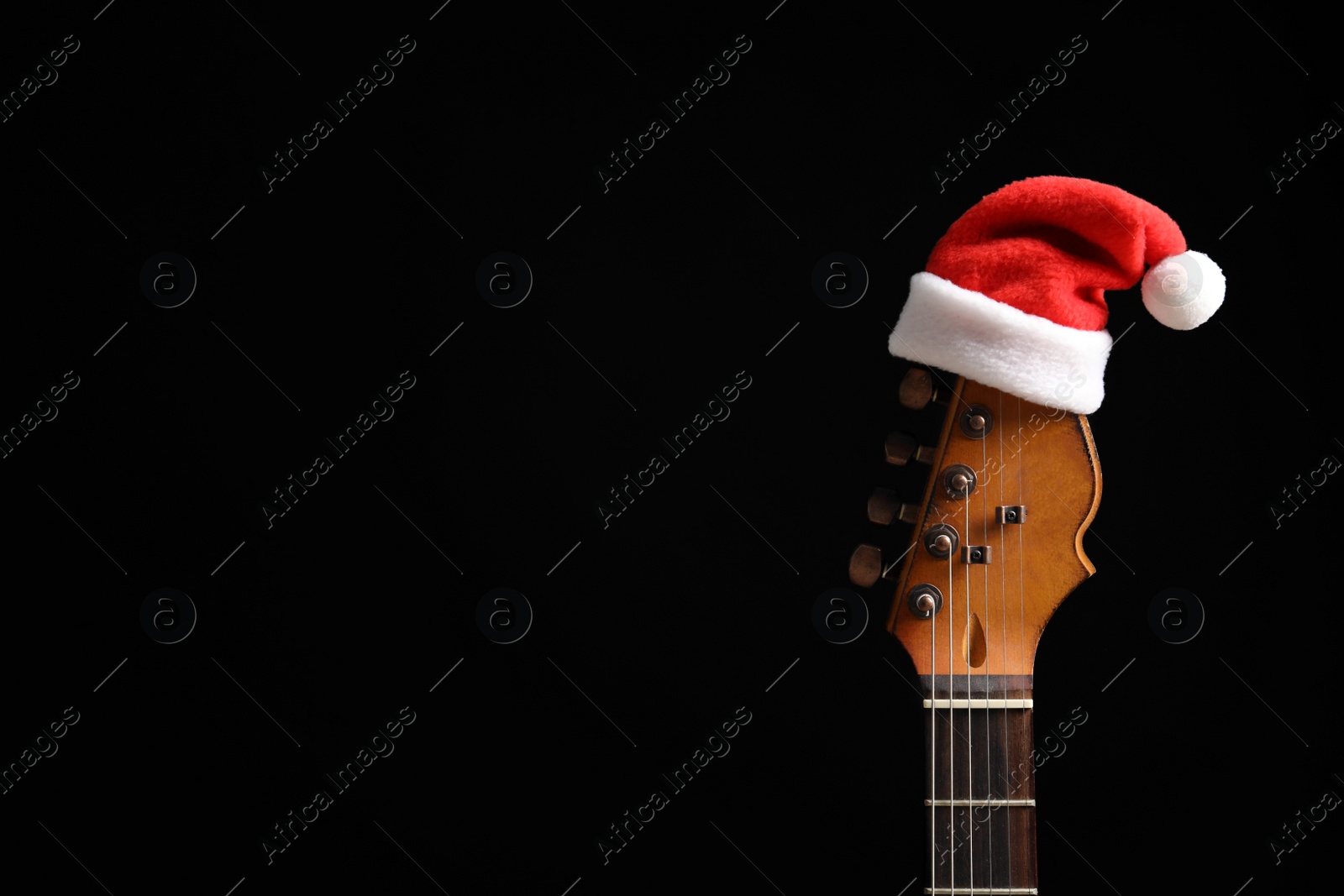 Photo of Guitar with Santa hat on black background. Christmas music concept