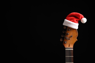 Photo of Guitar with Santa hat on black background. Christmas music concept