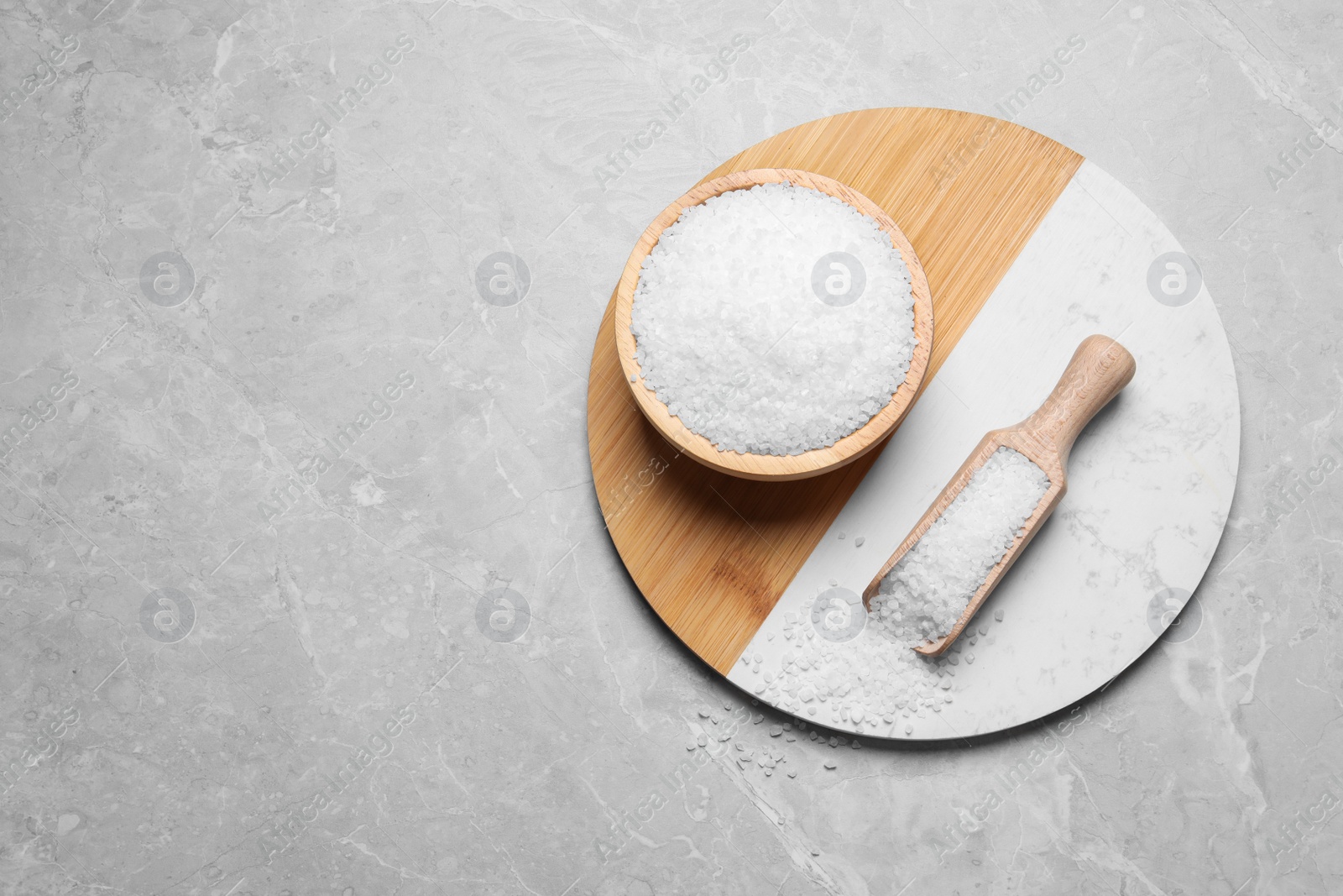 Photo of Wooden bowl and scoop with natural sea salt on light grey table, top view. Space for text