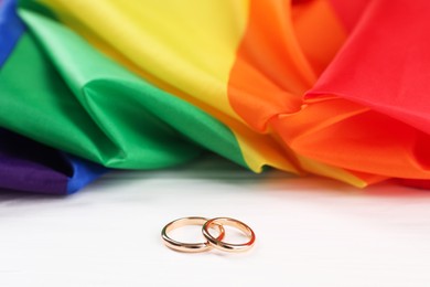 Rainbow LGBT flag and wedding rings on white wooden table, closeup