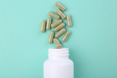 Bottle and vitamin capsules on turquoise background, top view