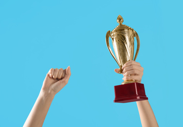 Photo of Woman holding gold trophy cup on light blue background, closeup