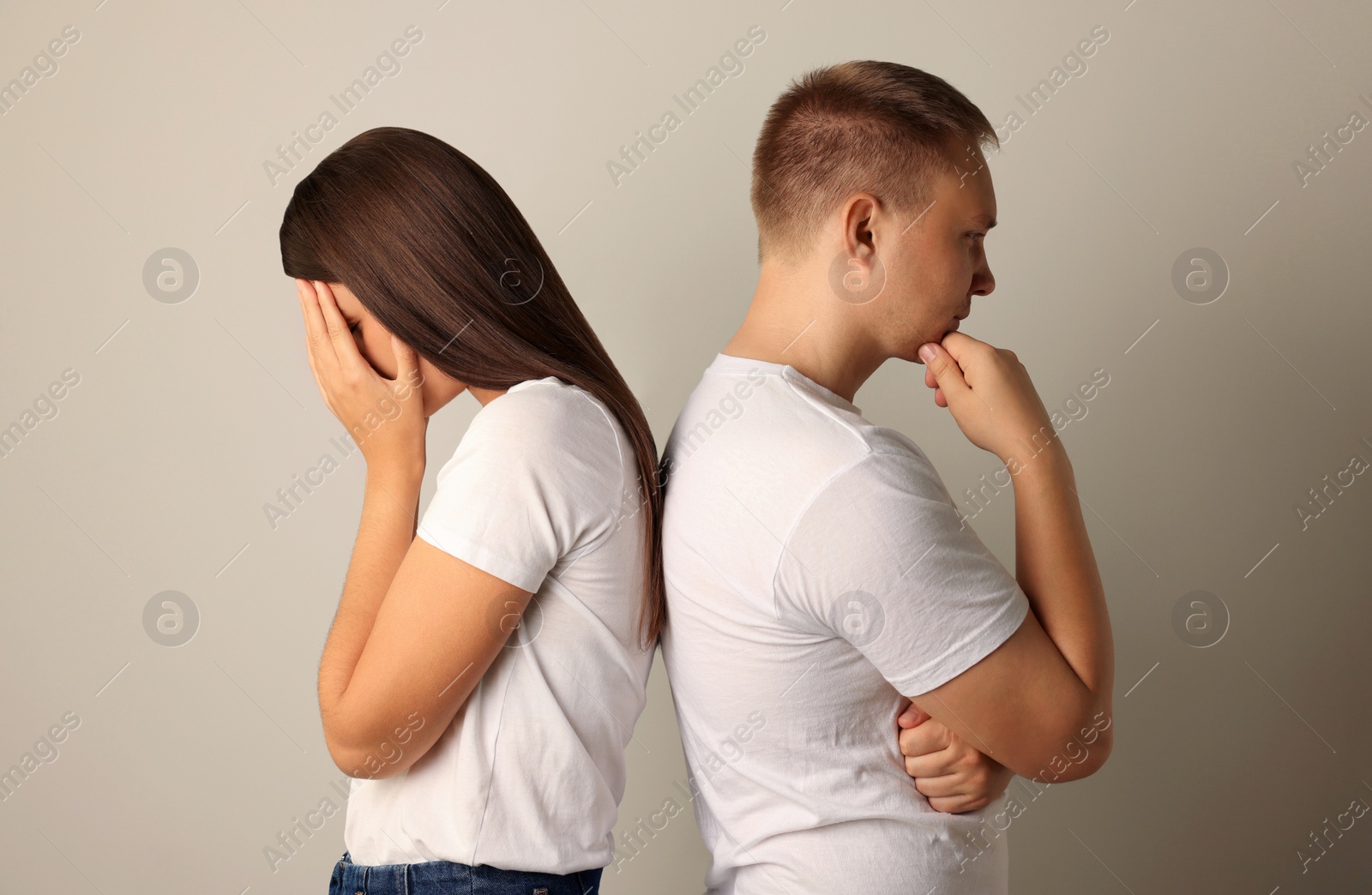 Photo of Unhappy young couple turning their backs on each other against light background