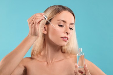 Beautiful woman applying cosmetic serum onto her face on light blue background