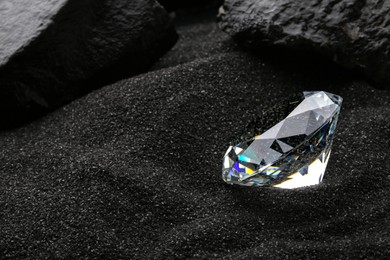 Photo of Beautiful shiny diamond on decorative black sand. Space for text