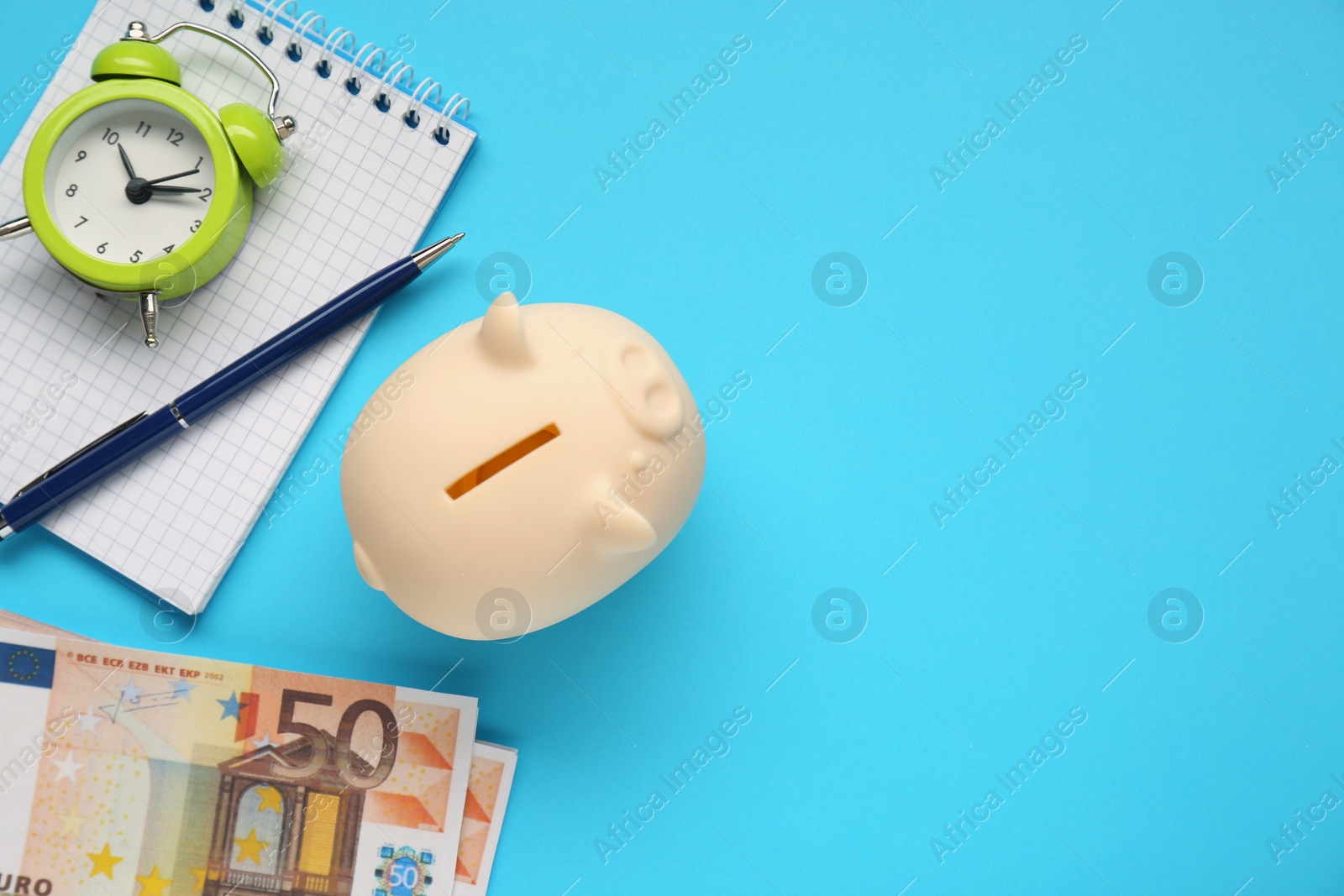 Photo of Piggy bank, alarm clock, notebook and banknotes on light blue background, flat lay. Space for text