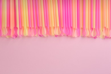 Heap of colorful plastic drinking straws on pink background, flat lay. Space for text