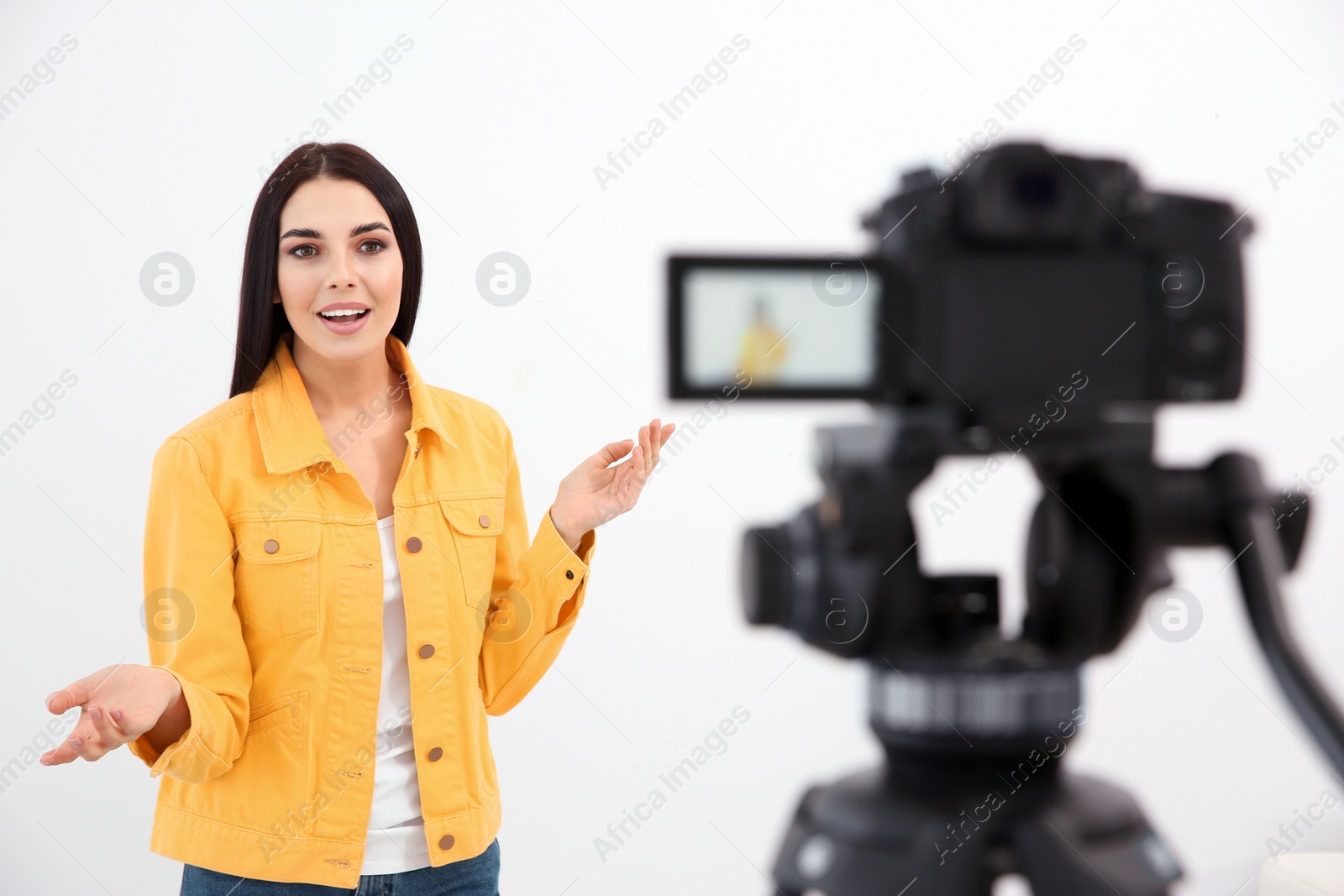 Photo of Young blogger recording video on camera against white background