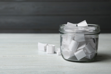 Glass jar with paper pieces on white wooden table, space for text