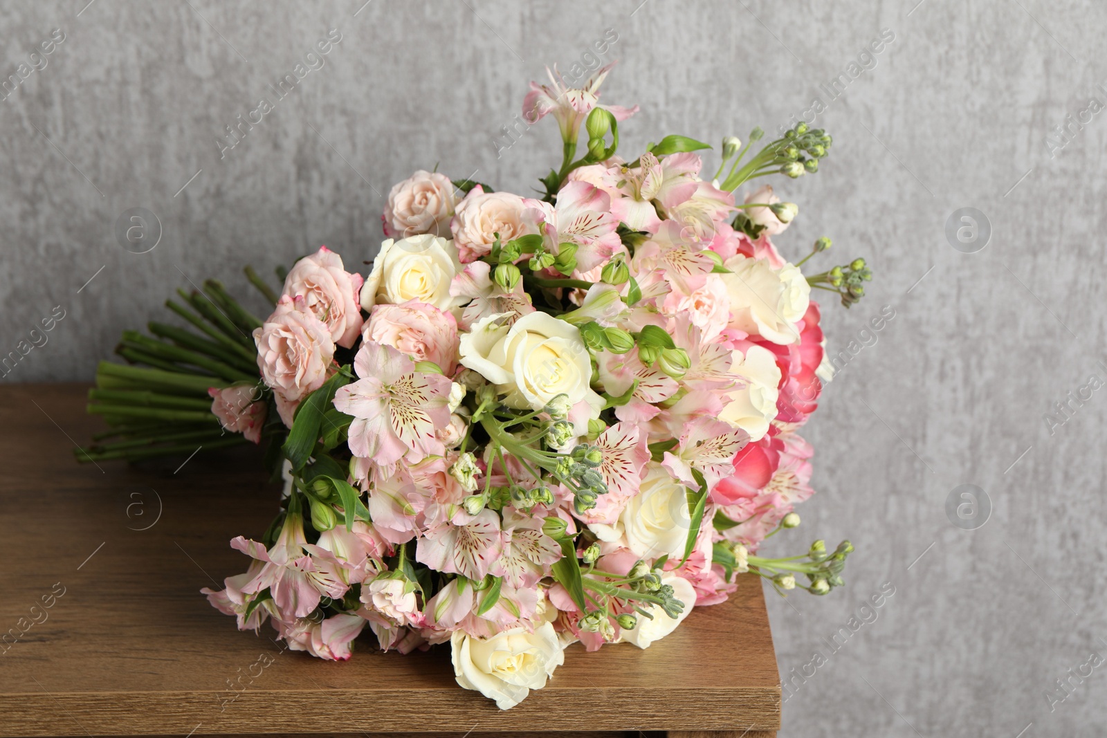 Photo of Beautiful bouquet of fresh flowers on wooden table near grey wall