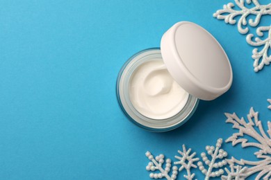 Photo of Jar of hand cream and snowflakes on light blue background, flat lay with space for text. Winter skin care