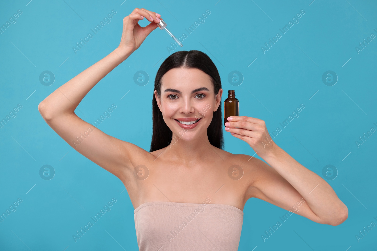 Photo of Beautiful woman applying hair serum on light blue background. Cosmetic product