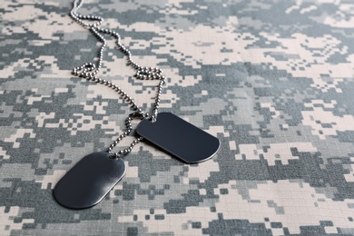 Metal military ID tags on camouflage background. Space for text