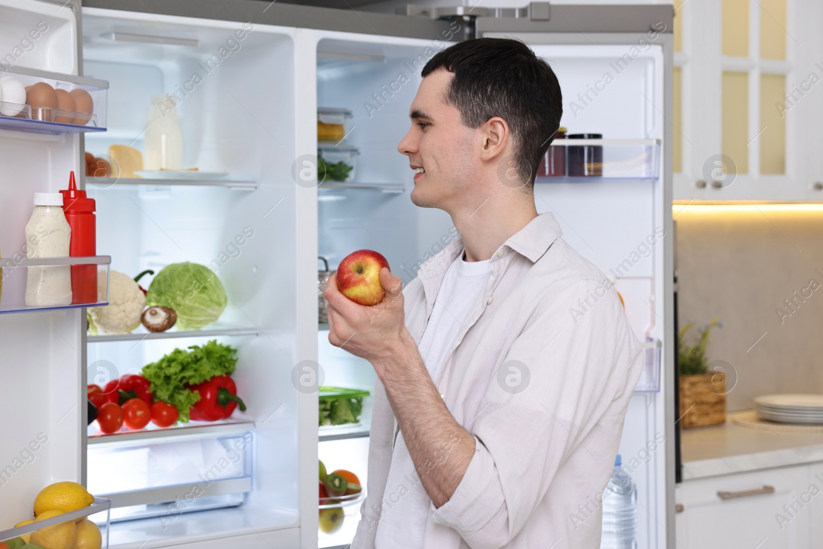 Photo of Happy man holding apple near refrigerator in kitchen