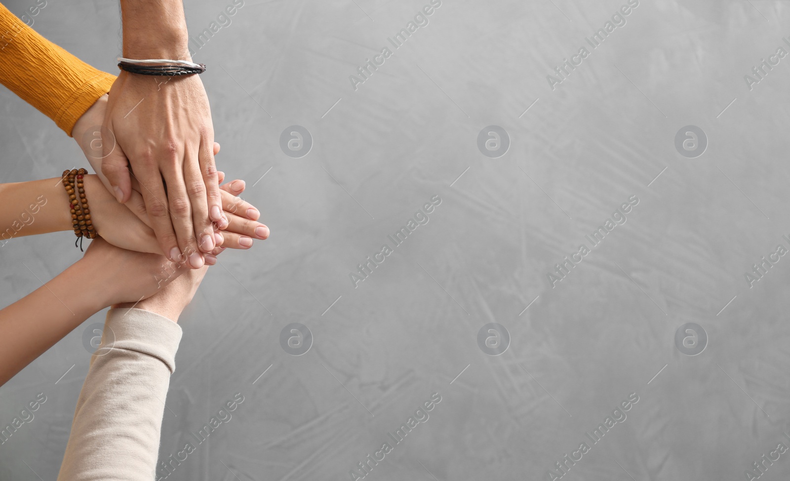 Photo of People holding hands together over grey stone background, top view with space for text. Unity concept