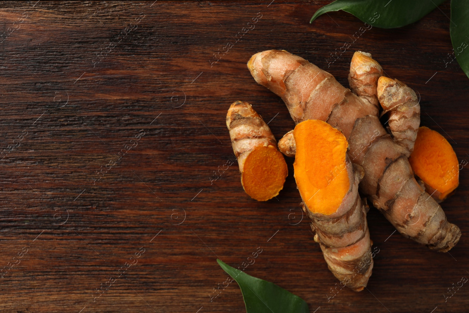 Photo of Fresh turmeric roots and leaves on wooden table, flat lay. Space for text