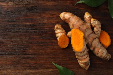 Fresh turmeric roots and leaves on wooden table, flat lay. Space for text