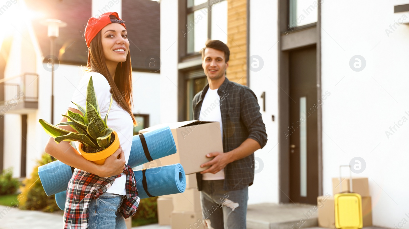 Photo of Happy couple with moving boxes and household stuff near their new house on sunny day