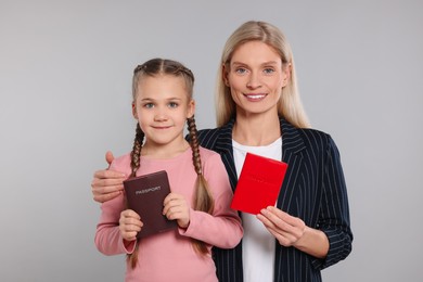 Photo of Immigration. Happy woman and her daughter with passports on gray background