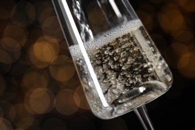 Photo of Pouring champagne into glass against blurred lights, closeup