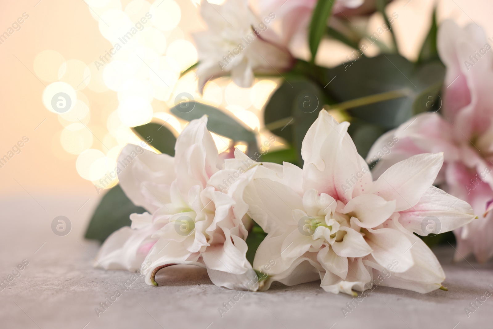 Photo of Bouquet of beautiful lily flowers on table against beige background with blurred lights, closeup