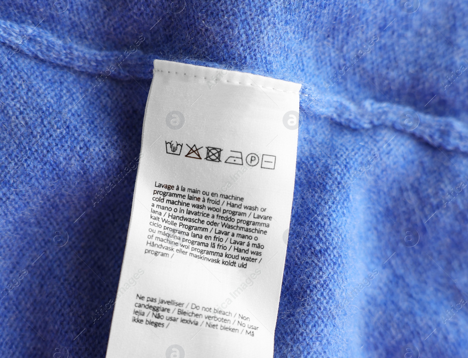 Photo of Clothing label in different languages on blue garment, top view