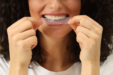 Photo of Young woman applying whitening strip on her teeth, closeup