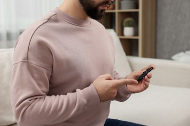 Photo of Diabetes test. Man checking blood sugar level with lancet pen on sofa, closeup