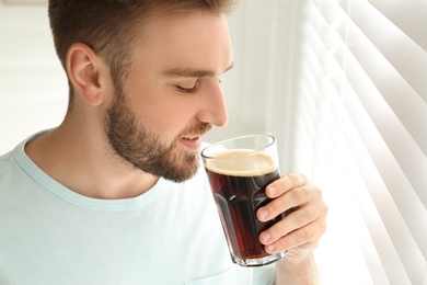 Photo of Handsome man with cold kvass indoors. Traditional Russian summer drink