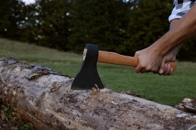 Photo of Man with axe cutting log outdoors, closeup