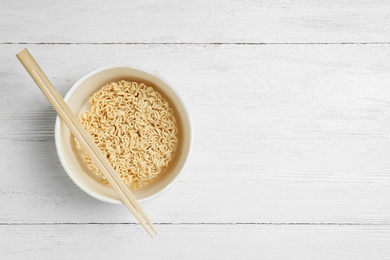 Photo of Cup of instant noodles with chopsticks on white wooden background, top view. Space for text
