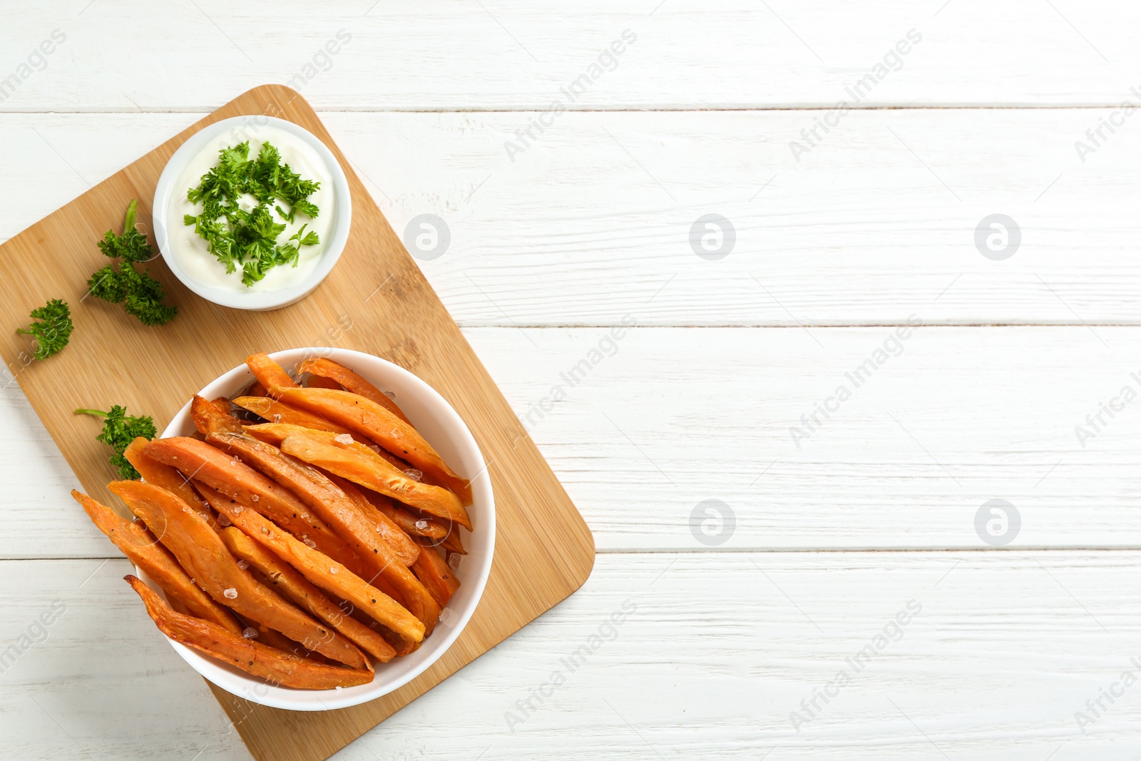 Photo of Bowl with tasty sweet potato fries and sauce on wooden background, top view. Space for text