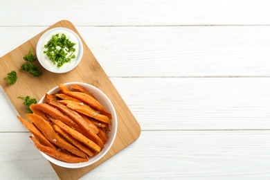 Bowl with tasty sweet potato fries and sauce on wooden background, top view. Space for text