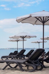 Photo of Many beautiful white umbrellas and black sunbeds on beach