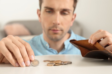 Photo of Sad man putting coins into wallet at table