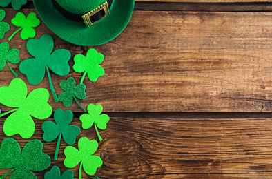 Photo of Green leprechaun hat and clover leaves on wooden table, flat lay with space for text. St. Patrick's Day celebration