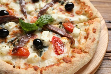 Photo of Tasty pizza with anchovies, basil and olives on wooden table, closeup