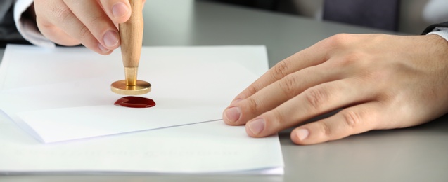 Image of Notary stamping document at table, closeup. Banner design