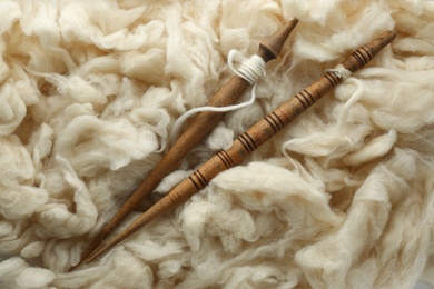 Photo of Soft white wool with spindles as background, top view
