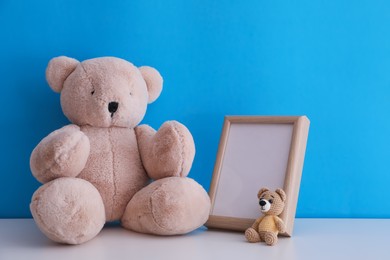 Photo of Empty photo frame and toy bears on white table near light blue wall. Space for design