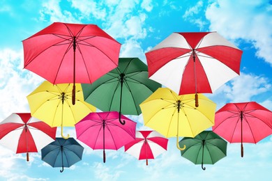 Image of Group of different colorful umbrellas against blue sky with white clouds on sunny day