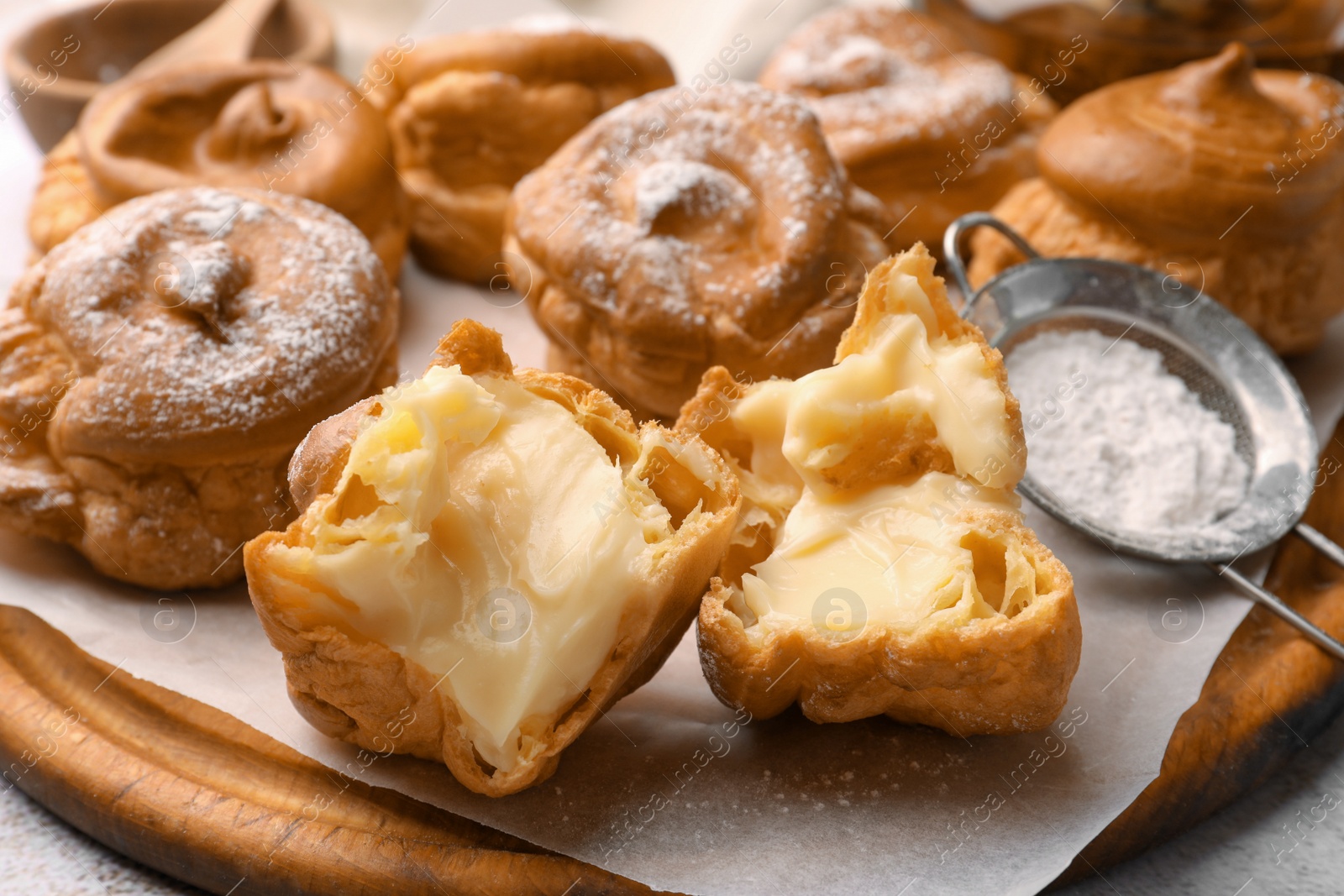 Photo of Delicious profiteroles filled with cream on wooden board, closeup